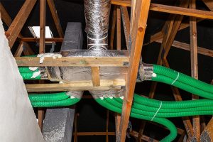 An exposed home attic space featuring a newly installed residential HVAC ventilation system with insulated silver main plenums and bright green flexible air distribution ductwork routed through wooden roof trusses.